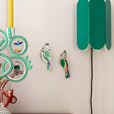 Studio Roof forest crests wall decorations available at Babipur. Hanging on a lightly coloured wall with a retro green lamp on the side