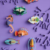 A group of Studio Roof sealife animal wall decorations available at Babipur hanging on a purple coloured wall including a lagoon triggerfish