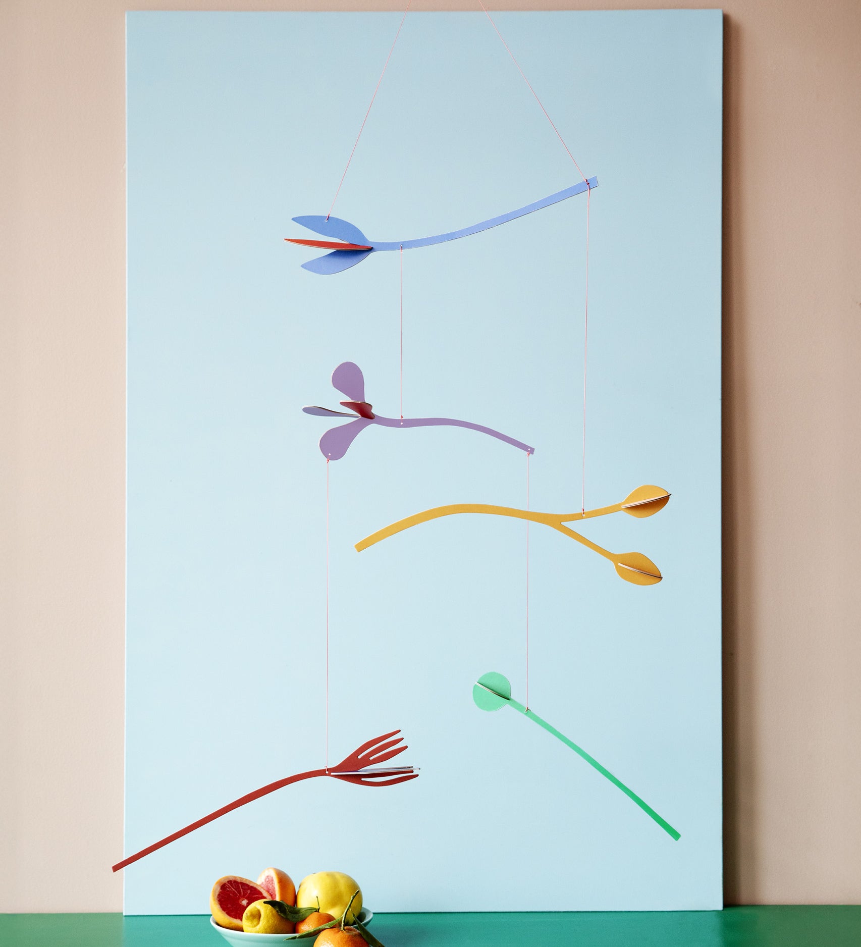 A Studio Roof cardboard Cordelia floral art mobile hanging over a table. This multicoloured floral DIY cardboard set is available at Babipur.