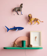 Studio Roof shark wall decoration available at Babipur hanging on a pink wall next to a lion and zebra DIY kit. 