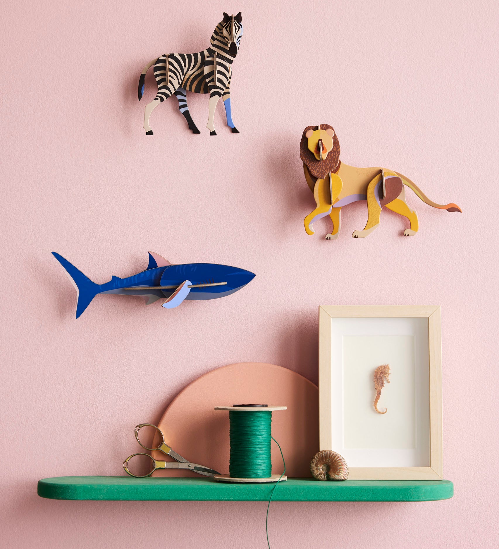 Studio Roof shark wall decoration available at Babipur hanging on a pink wall next to a lion and zebra DIY kit. 