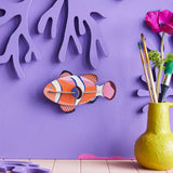 Studio Roof small clownfish wall decoration available at Babipur hanging on a purple wall next to a yellow vase