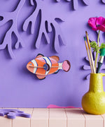 Studio Roof small clownfish wall decoration available at Babipur hanging on a purple wall next to a yellow vase