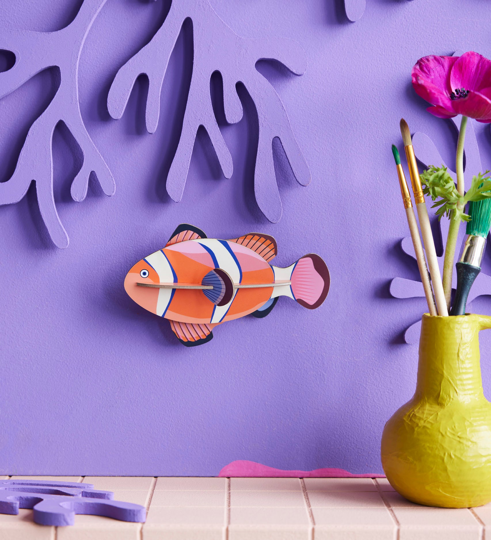 Studio Roof small clownfish wall decoration available at Babipur hanging on a purple wall next to a yellow vase