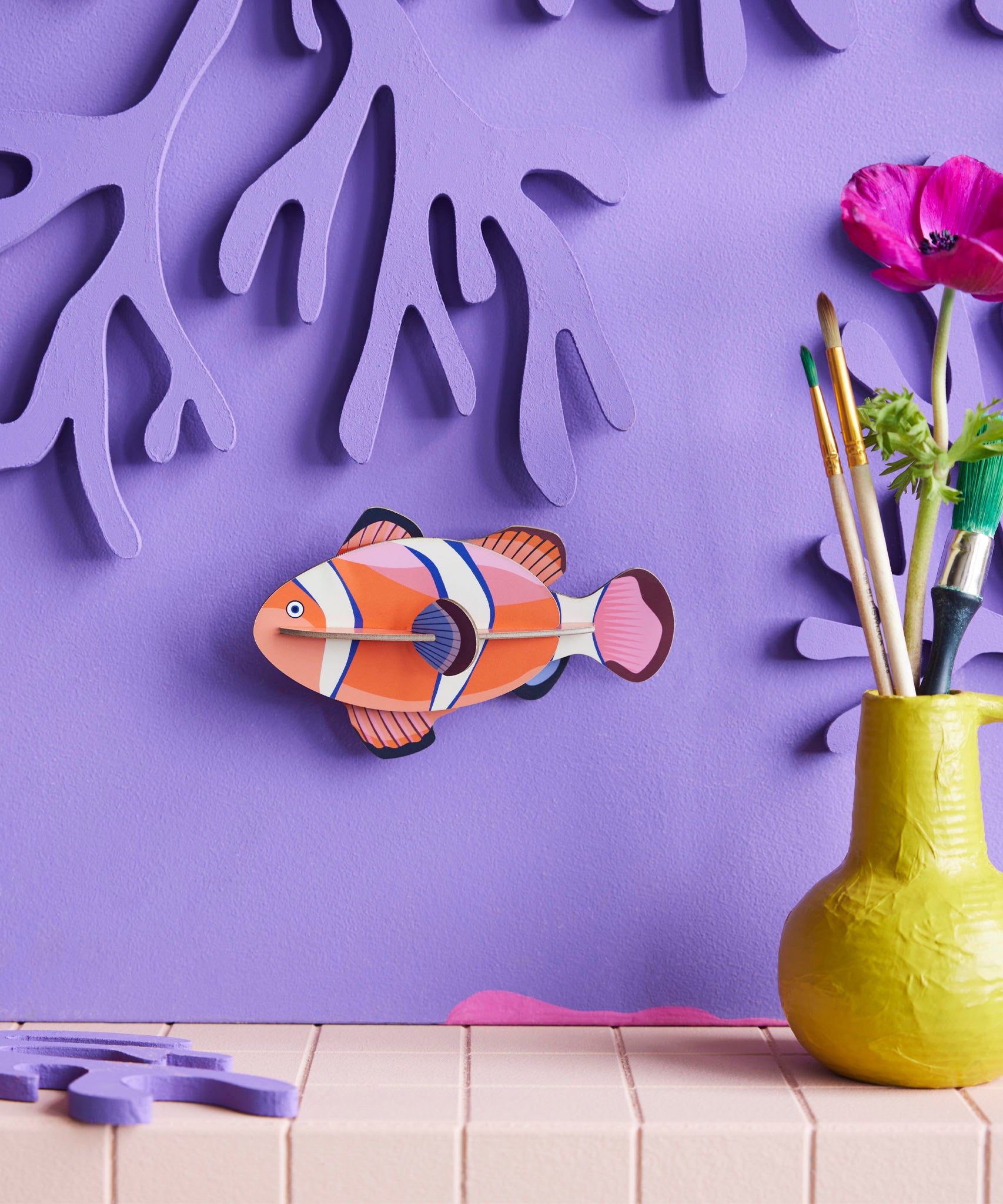 Studio Roof small clownfish wall decoration available at Babipur hanging on a purple wall next to a yellow vase