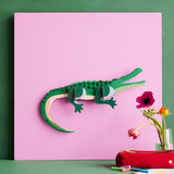 Studio Roof tall crcocdile wall decoration available at Babipur hanging on a pink board against a green wall 
