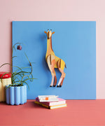Studio Roof tall giraffe wall decoration available at Babipur hanging on a blue board above a desk