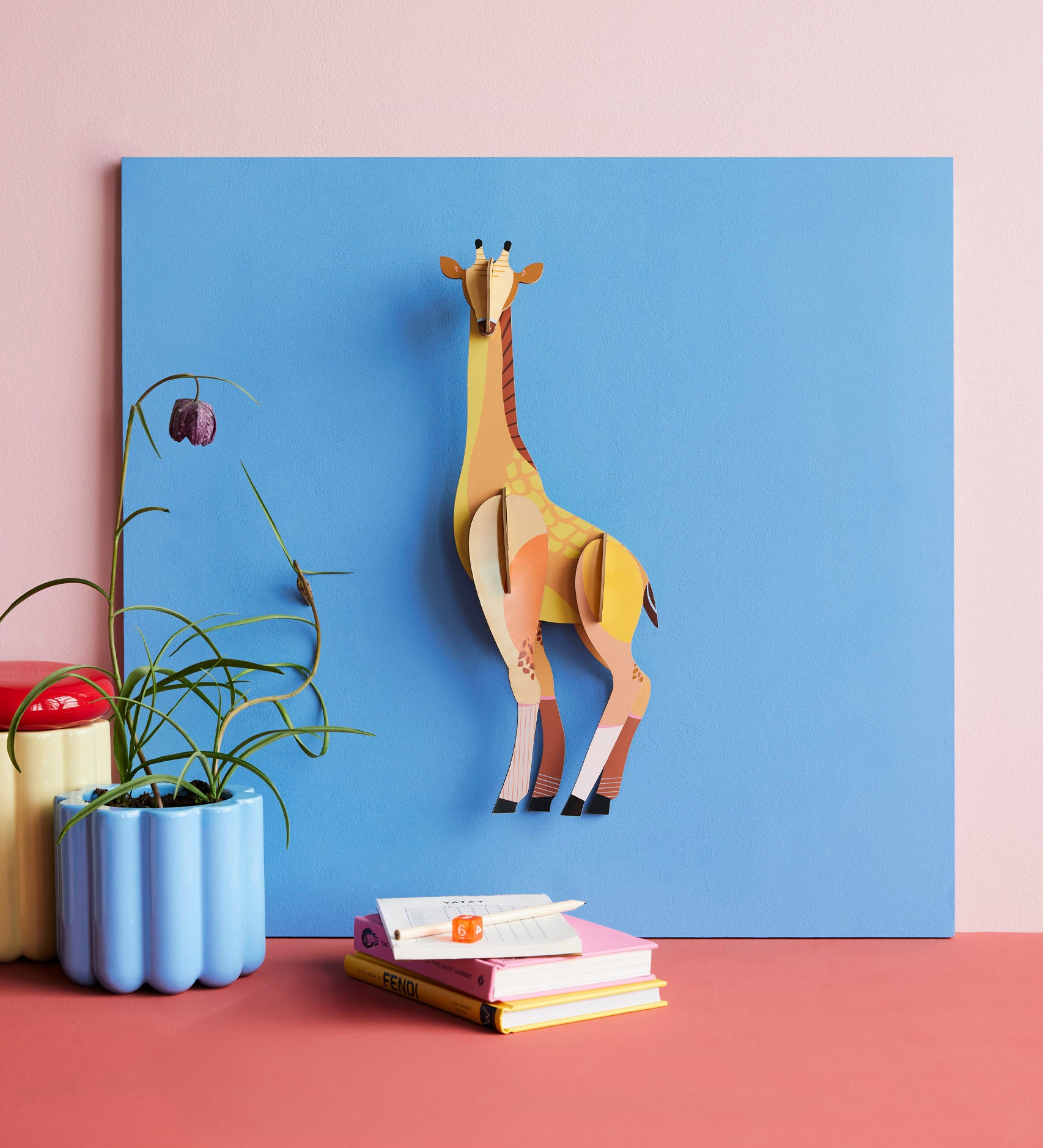 Studio Roof tall giraffe wall decoration available at Babipur hanging on a blue board above a desk