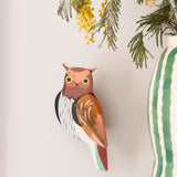 Studio Roof tawny owl wall decoration available at Babipur. Hanging on a lightly coloured wall with a striped vase in front.