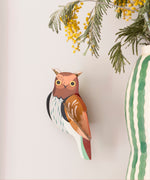 Studio Roof tawny owl wall decoration available at Babipur. Hanging on a lightly coloured wall with a striped vase in front.