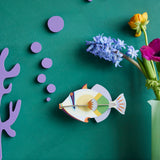 Studio Roof lagoon triggerfish wall decoration available at Babipur hanging on a green wall next to a green vase