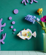 Studio Roof lagoon triggerfish wall decoration available at Babipur hanging on a green wall next to a green vase