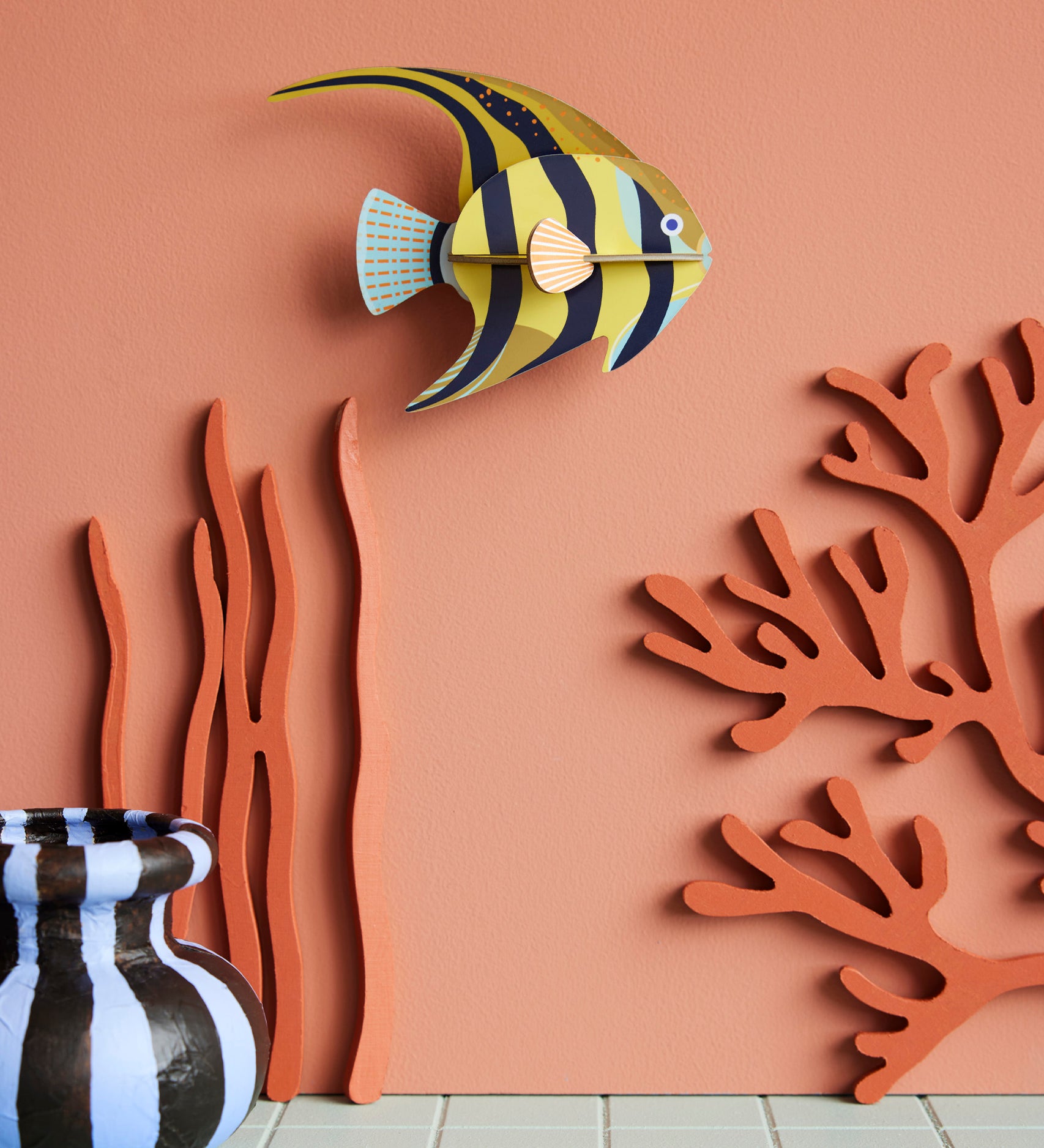 Studio Roof small angelfish wall decoration available at Babipur hanging on a lightly coloured wall next to a striped vase