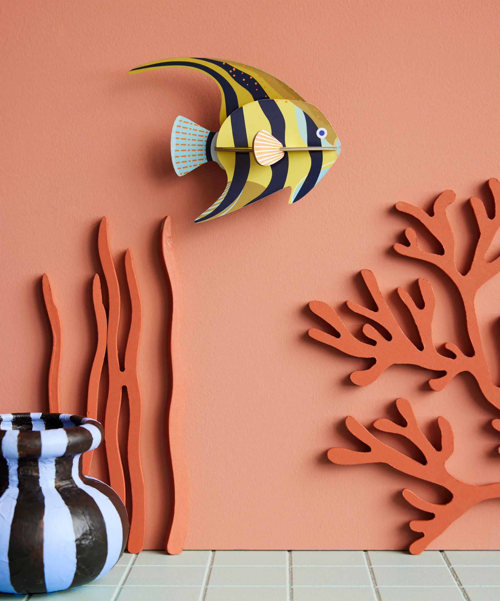 Studio Roof small angelfish wall decoration available at Babipur hanging on a lightly coloured wall next to a striped vase