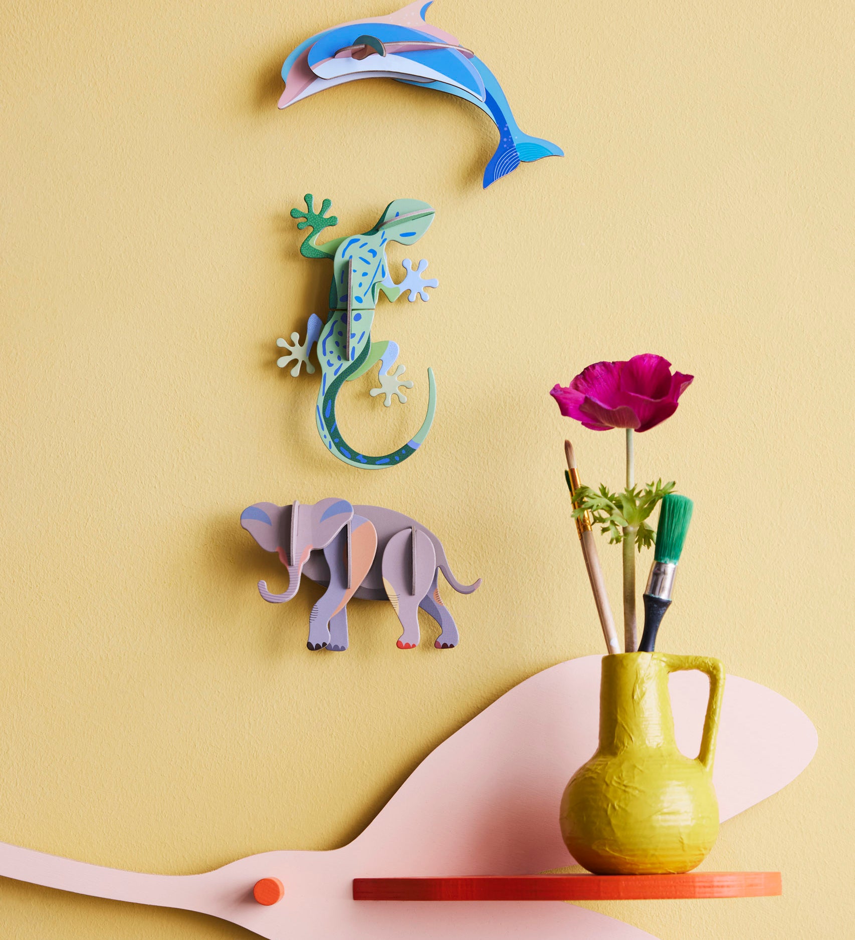 Studio Roof dolphin wall decoration available at Babipur hanging on a yellow wall next to a gecko and elephant DIY hanging decoration