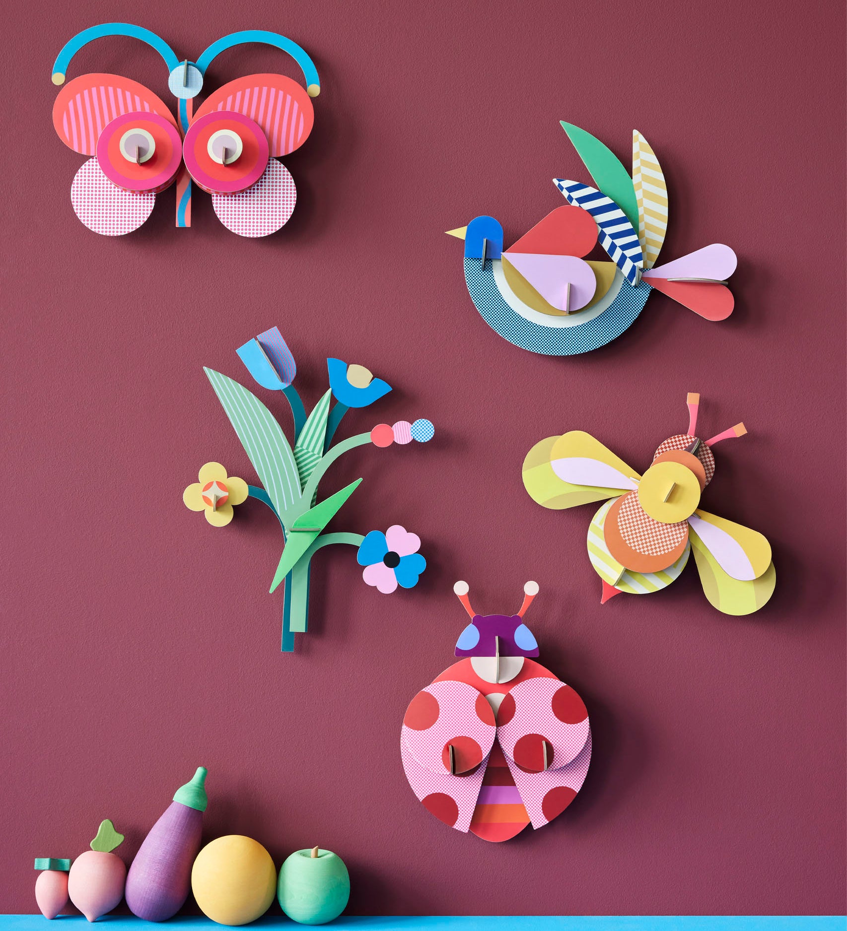 A group of wall decorations from the collaboration with Studio Roof and Zoe Miller available at Babipur. Decorations are hanging on a wall above wooden vegetables 