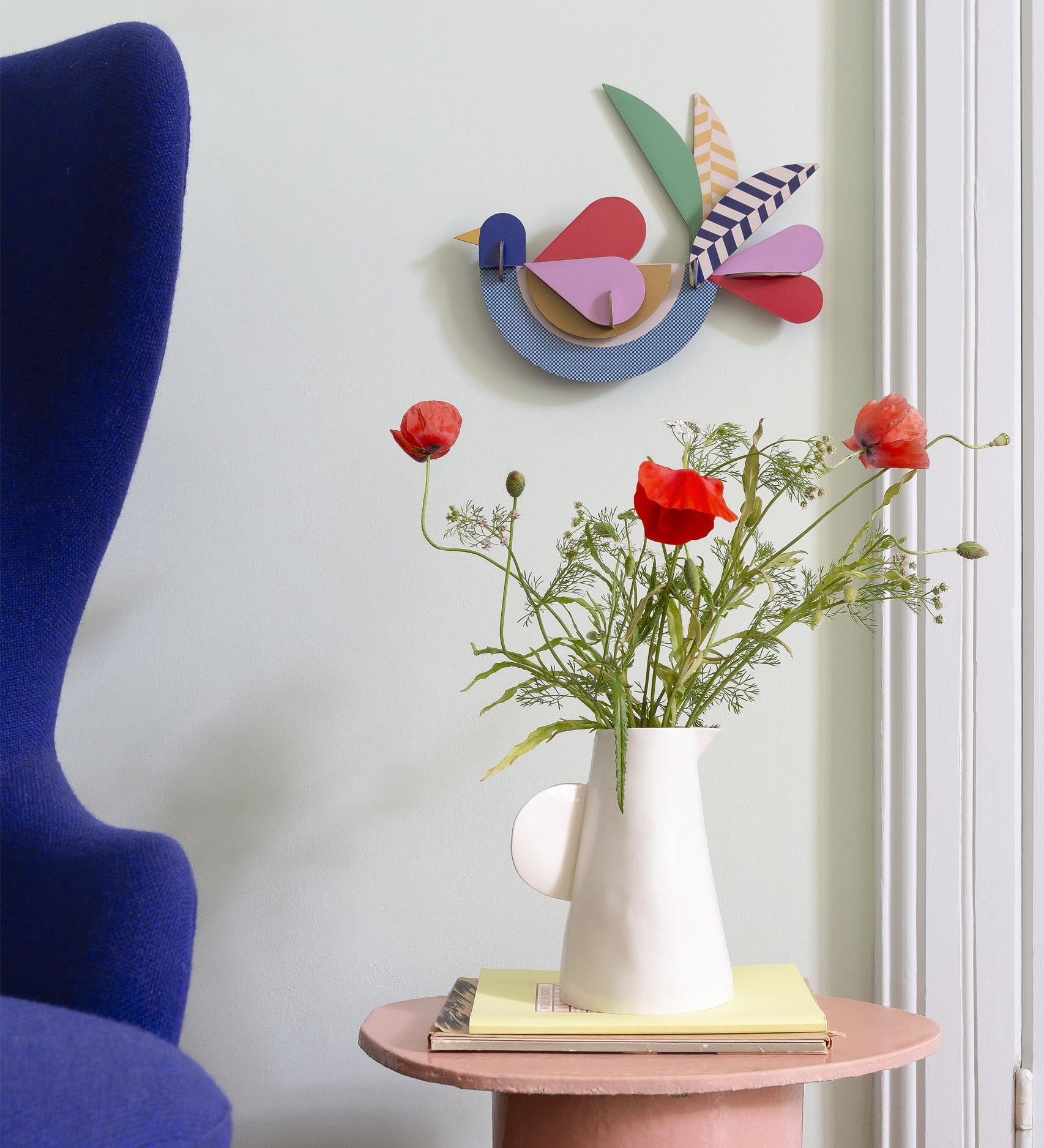 Feathery bird wall decoration available at Babipur hanging on a wall above a white vase with flowers. A Studio roof collaboration with artist Zoe Miller. 