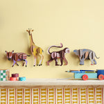3 Studio Roof 3D Cardboard Models of Wildlife Animals on a yellow wall - the Boar Piglet, Giraffe, Monkey and the Elephant. They are surrounded by decorative objects.