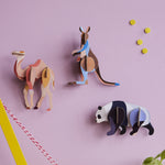 3 Studio Roof 3D Cardboard Models of Wildlife Animals on a lilac wall - the Camel, Kangaroo and the Panda. They are surrounded by decorative objects.