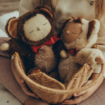 Olli Ella Cozy Dinkum Dolls Teddy Twiggy and Teddy Crumble together, sat in an Olli Ella Pionsettia Basket in natural, which is being held by a child
