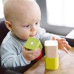 A baby playing with blocks from the  Tegu Baby's First Magnetic Blocks which is set on a wooden table. The baby is sat in a high chair at the table