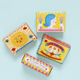 A group of The Printed Peanut sunshine natural handmade soaps showing their decorated packaging box against a blue background.