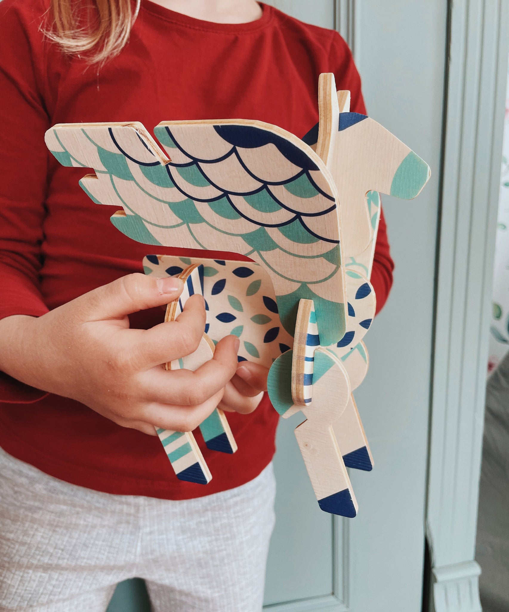 A close up of a child holding a completed Tobe Pegasus Fantasy Animals wooden Puzzle that's available at Babipur showing scale. 