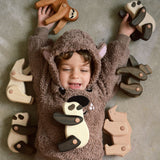 A child lying on the floor with a collection of the different Tobe wooden animals available at Babipur including a sloth, polar bear, panda, gorilla and a rhino.