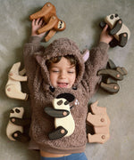 A child lying on the floor with a collection of the different Tobe wooden animals available at Babipur including a sloth, polar bear, panda, gorilla and a rhino.