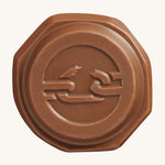 The front of the Tony's Chocolonely Tiny Mix chocolate button with the imprint of a broken chain on the front, to represent the breaking of slave labour. The image is on a cream background.