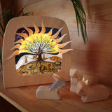 A cosy festive display with the Toverlux 12 holy nights sonne mond und erde silhouette inside a lamp. Silhouette features each date with a cut out for a message. Lamp is resting on a wooden surface next to Ostheimer wooden animal figures
