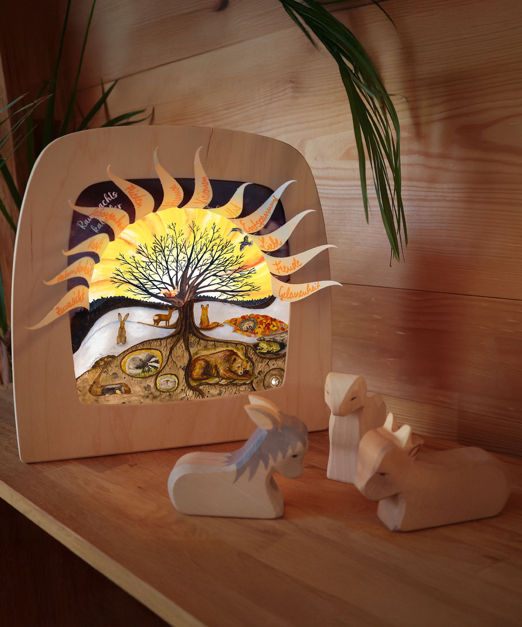 A cosy festive display with the Toverlux 12 holy nights sonne mond und erde silhouette inside a lamp. Silhouette features each date with a cut out for a message. Lamp is resting on a wooden surface next to Ostheimer wooden animal figures