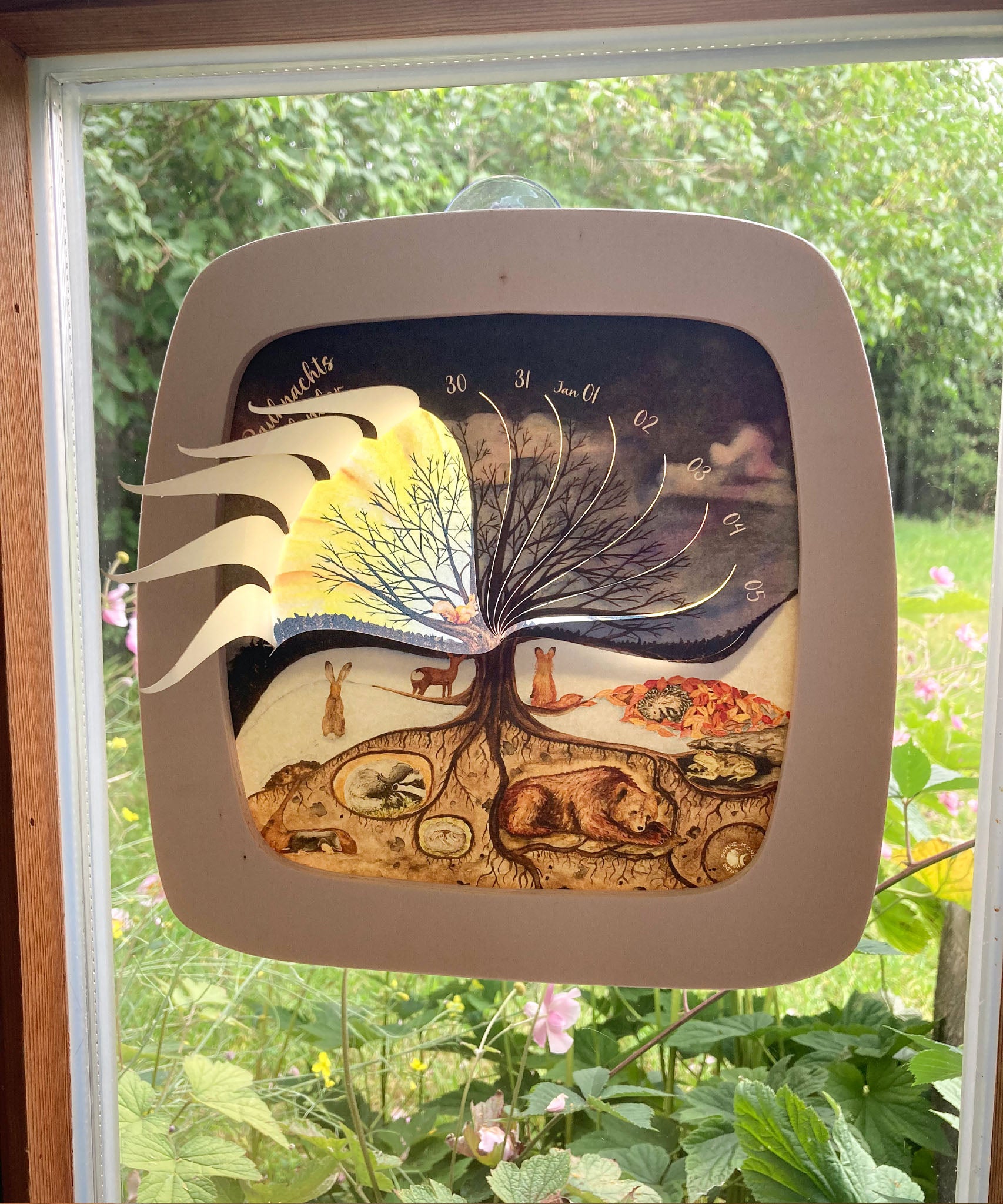 The Toverlux 12 holy nights sonne mond und erde silhouette inside a magic frame on a window showing the cut outs for each date folded out. Silhouette and frame are both available at Babipur