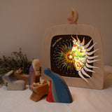 A cosy nativity inspired display with the Toverlux sonne mond und erde nativity advent calendar available at Babipur. Calendar some of the windows open revealing a lit up silhouette. 