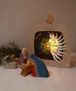 A cosy nativity inspired display with the Toverlux sonne mond und erde nativity advent calendar available at Babipur. Calendar some of the windows open revealing a lit up silhouette. 