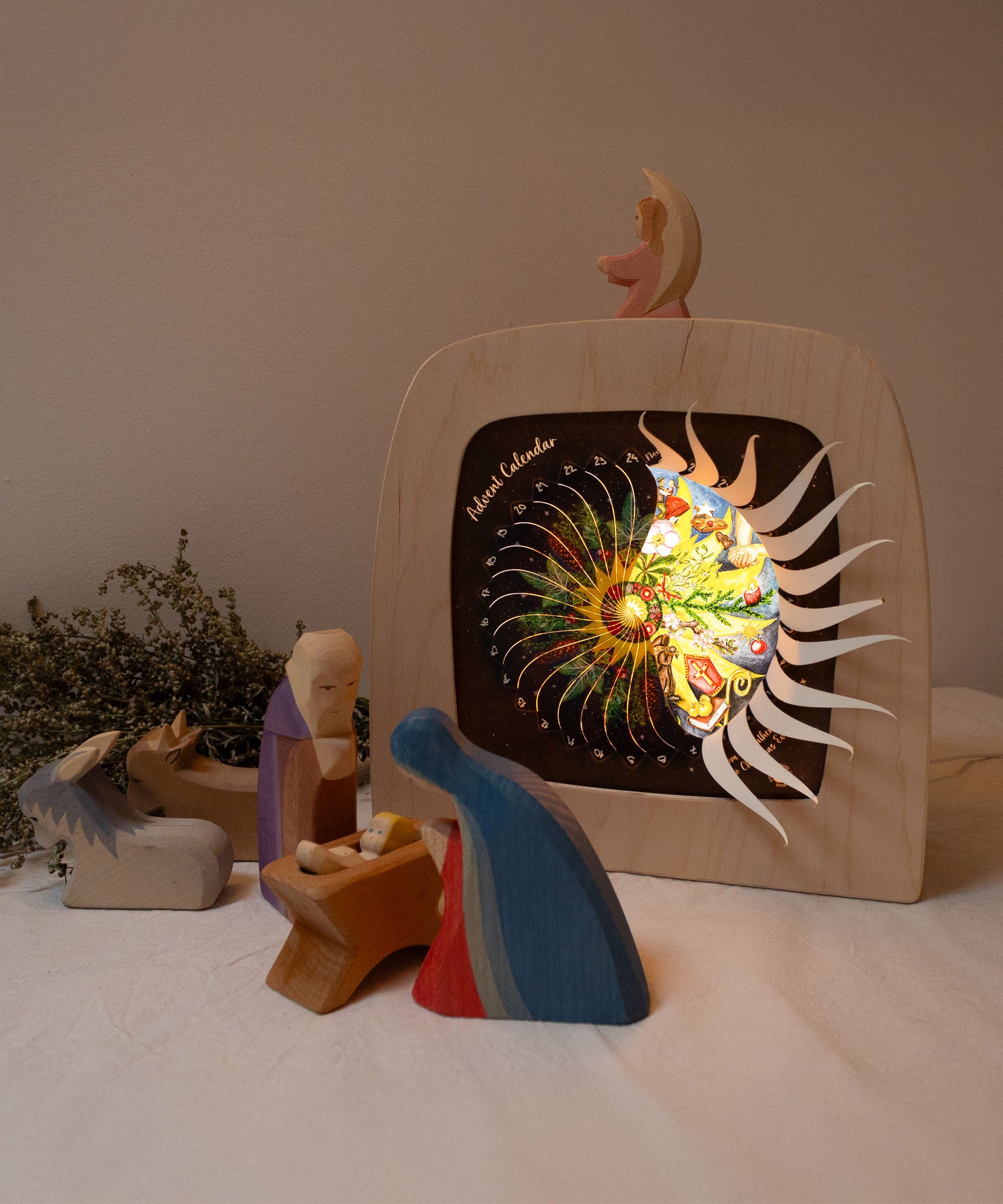 A cosy nativity inspired display with the Toverlux sonne mond und erde nativity advent calendar available at Babipur. Calendar some of the windows open revealing a lit up silhouette. 