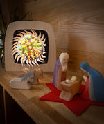 Mary and Joseph with baby Jesus and some animal wooden figures next to the Toverlux sonne mond und erde nativity advent calendar available at Babipur. Calendar has all of the windows open revealing a lit up silhouette. 