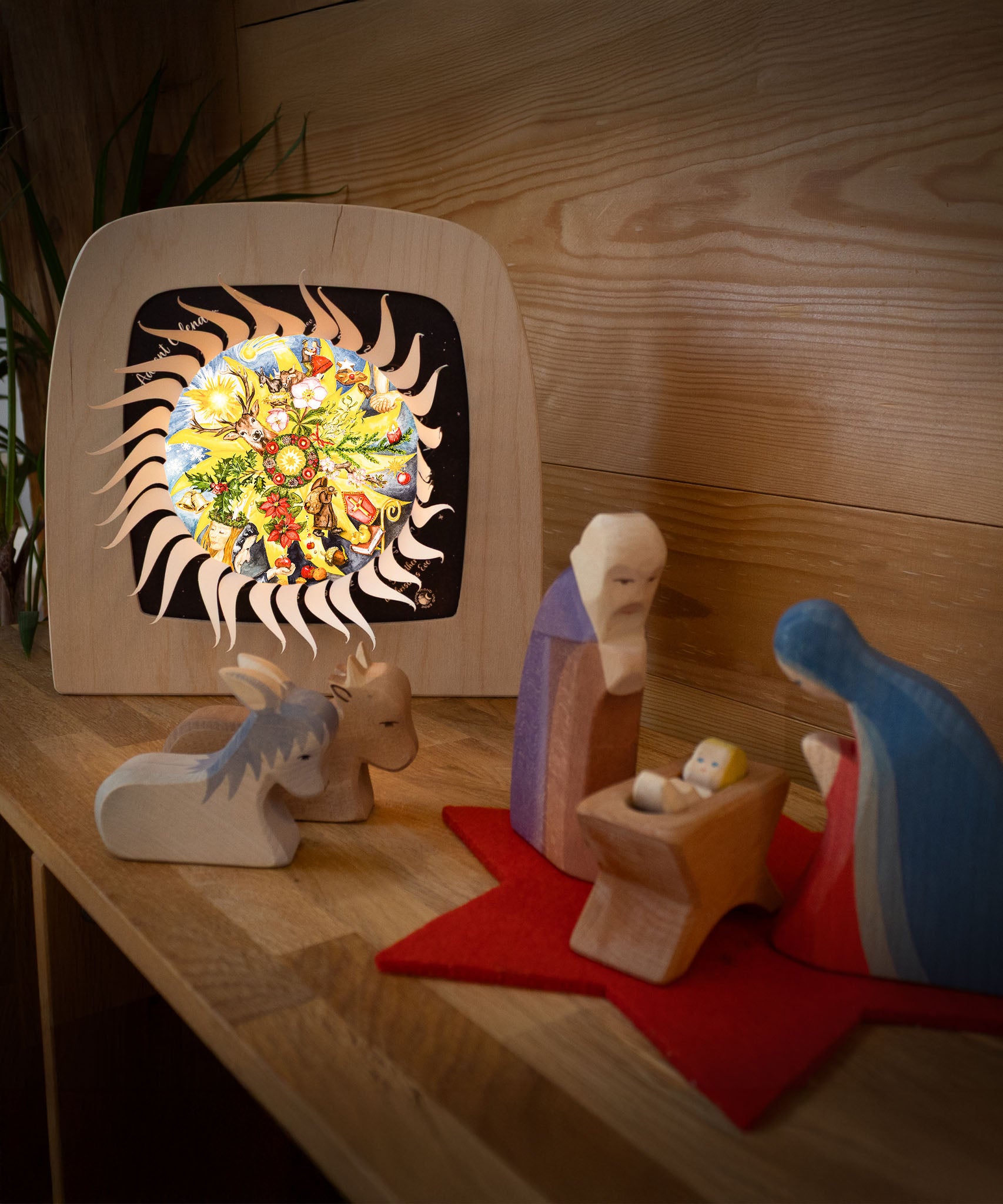 Mary and Joseph with baby Jesus and some animal wooden figures next to the Toverlux sonne mond und erde nativity advent calendar available at Babipur. Calendar has all of the windows open revealing a lit up silhouette. 