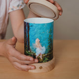 An adult holding lid on the Toverlux lantern ready to put on the Eentje Van Margo light wish illustration, both available at Babipur. 