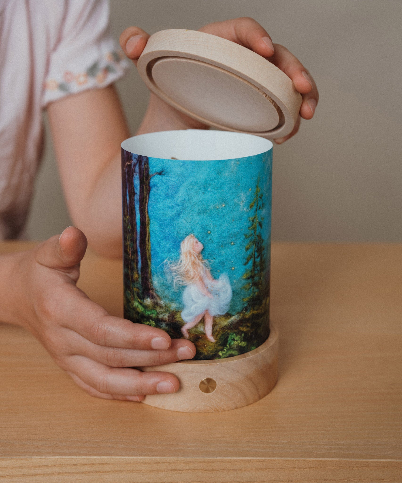 An adult holding lid on the Toverlux lantern ready to put on the Eentje Van Margo light wish illustration, both available at Babipur. 