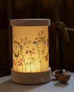 A lit up Toverlux Wooden Lantern night light with floral artwork, it has a re-chargeable non-wired wooden base.