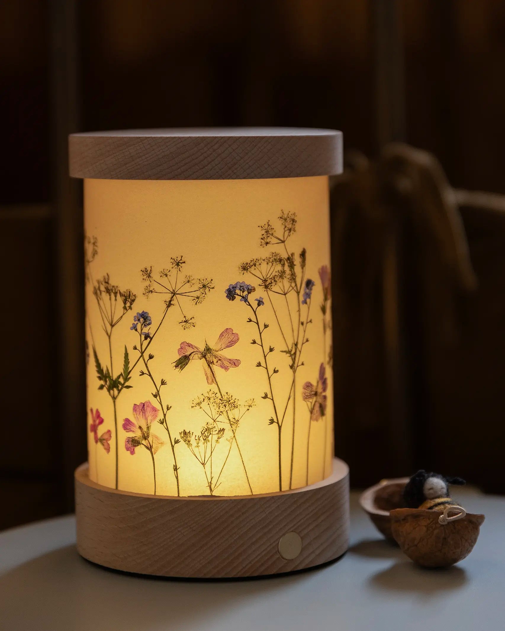A lit up Toverlux Wooden Lantern night light with floral artwork, it has a re-chargeable non-wired wooden base.