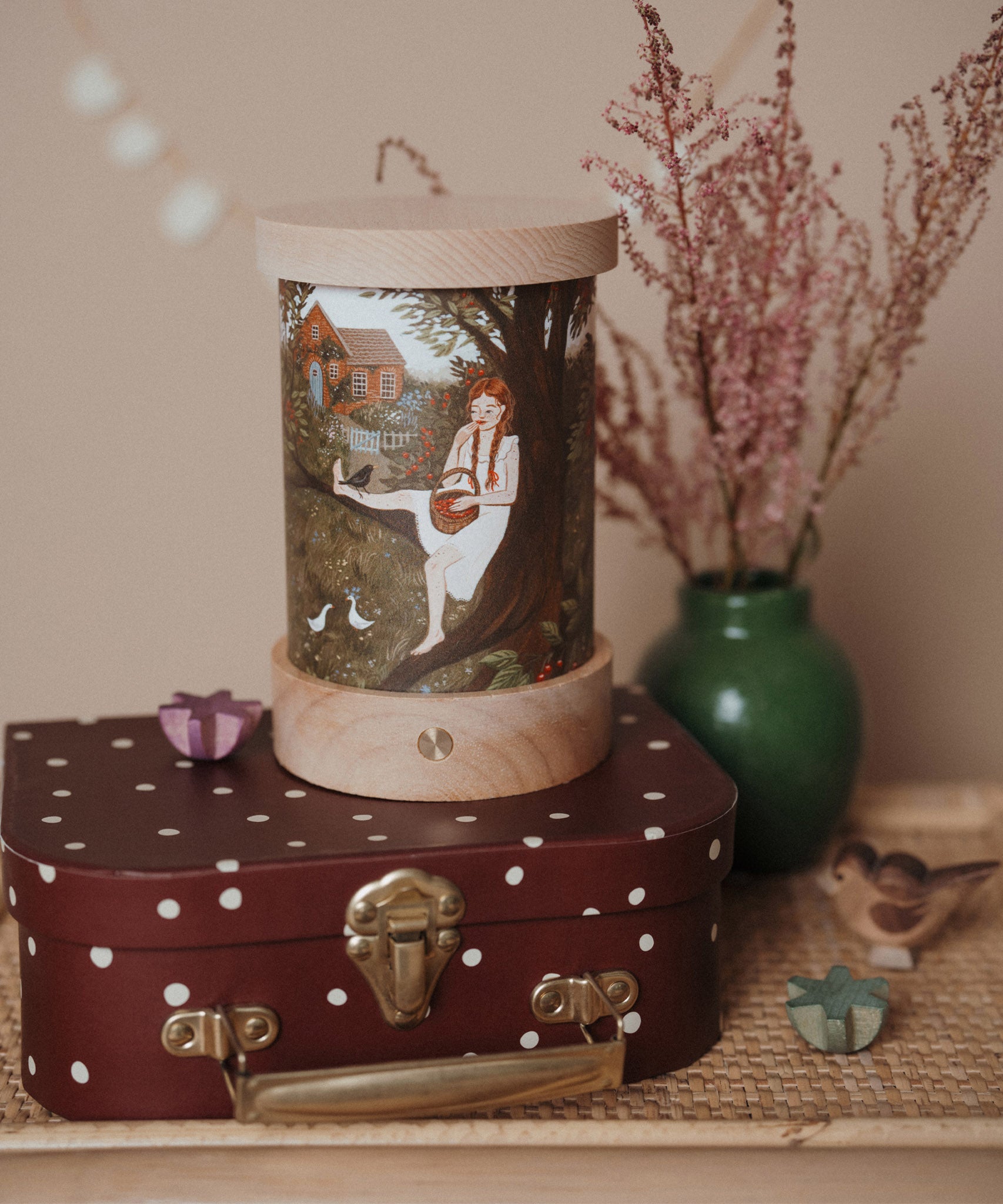 A retro cosy inspired display including the Toverlux rechargeable lantern on top of a mini suitcase with a Robin Pieterse light wish illustration inserted the lantern. Both the illustration and lantern are available at Babipur.