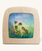 The Griswald Gnome Swing illustration by Daniela Drescher sat in a Toverlux Magic Lamp, on a cream background. The image shows Griswald Gnome sharing a birthday cake with a cat and a butterfly, whilst standing in a grassy green field with beautiful, colourful flowers.