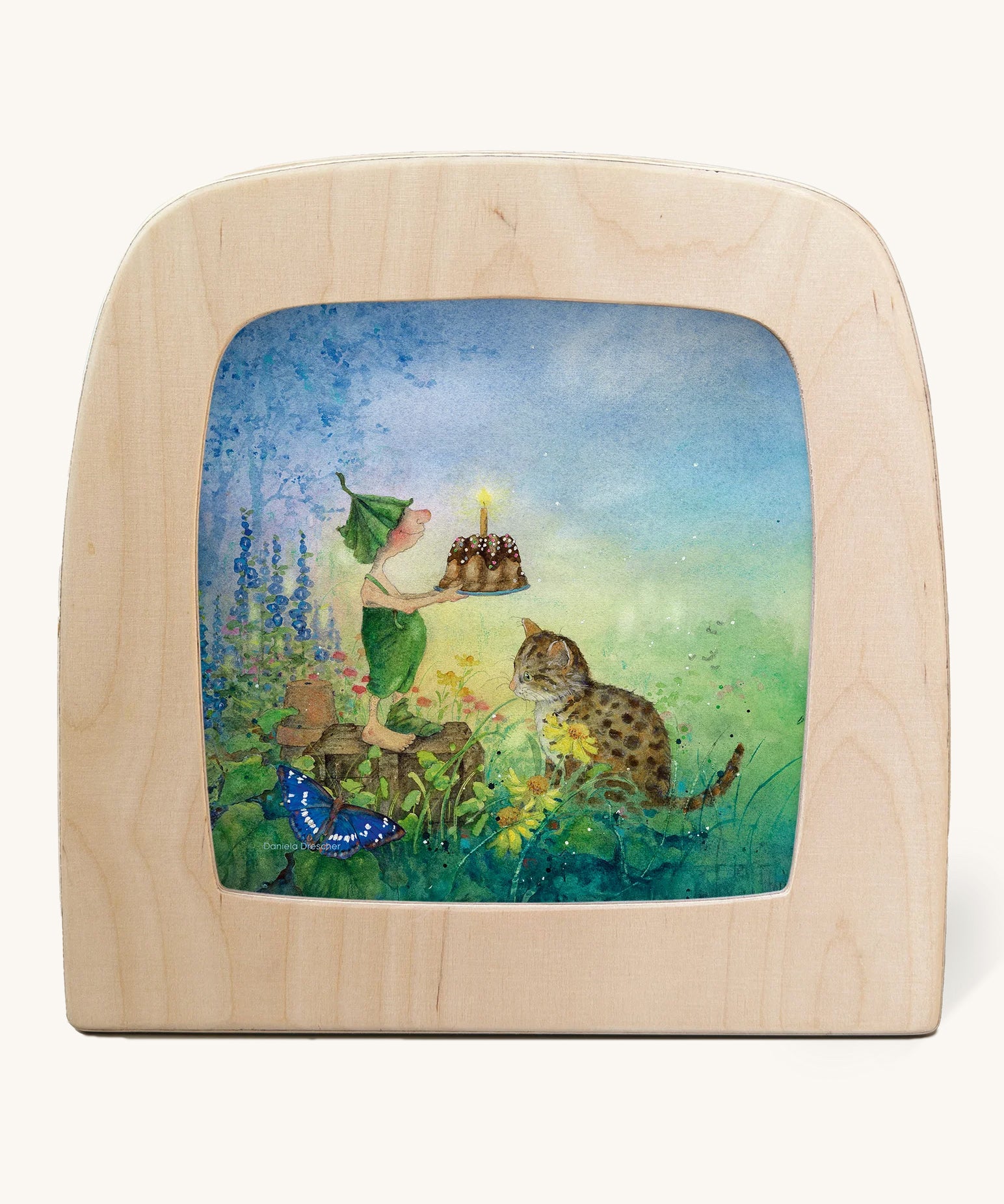 The Griswald Gnome Swing illustration by Daniela Drescher sat in a Toverlux Magic Lamp, on a cream background. The image shows Griswald Gnome sharing a birthday cake with a cat and a butterfly, whilst standing in a grassy green field with beautiful, colourful flowers.