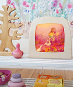 Toverlux Little goose silhouette inside a wooden magic lamb next to various wooden toys on a white shelf in the Babipur playroom. 