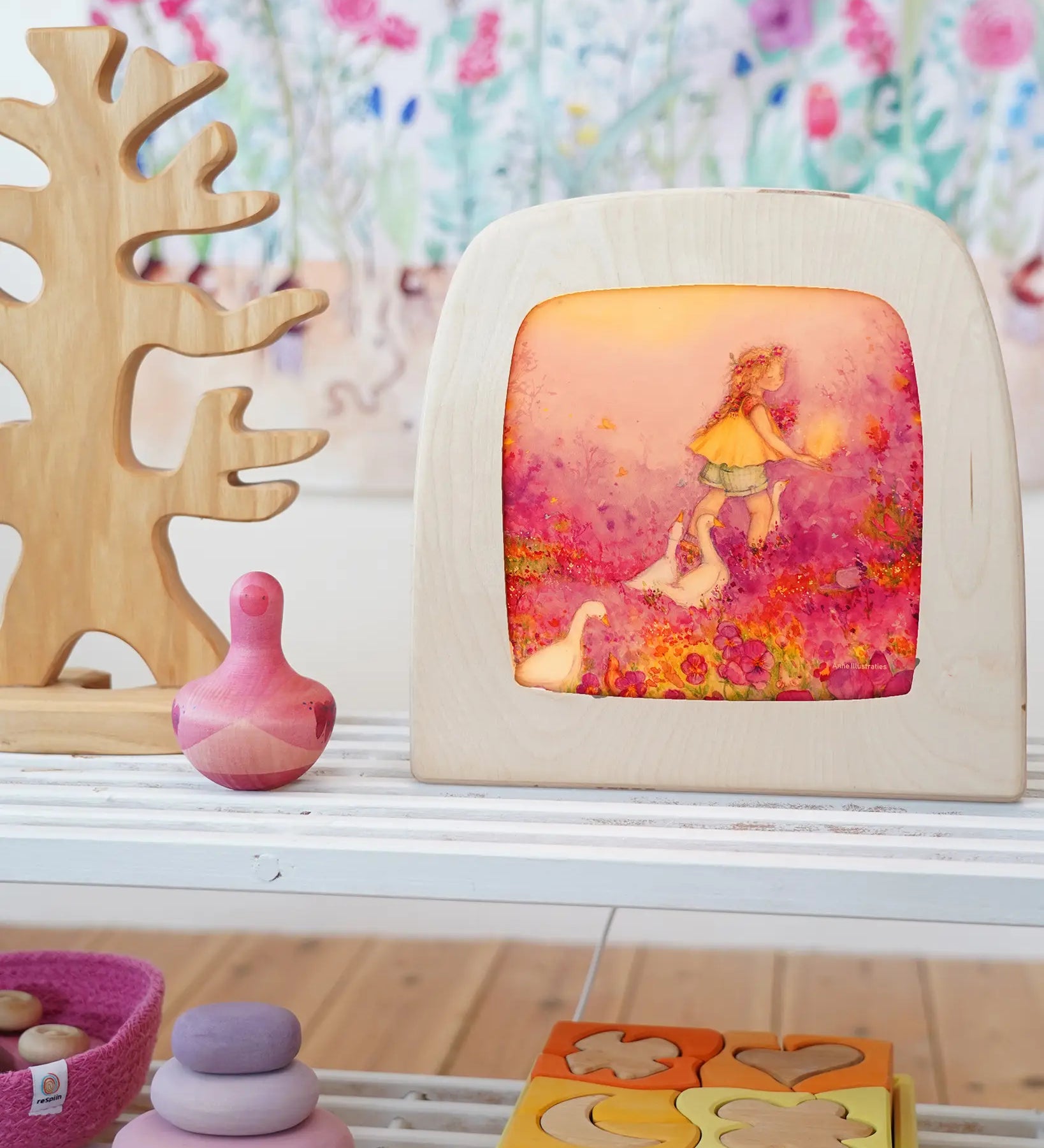 Toverlux Little goose silhouette inside a wooden magic lamb next to various wooden toys on a white shelf in the Babipur playroom. 