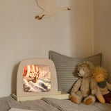 Toverlux Magic Lamp with artwork by Berit Strasser showing a Viking Ship sailing through the sea, on a child's bed next to a teddy bear and Nanchen Waldorf doll.