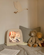 Toverlux Magic Lamp with artwork by Berit Strasser showing a Viking Ship sailing through the sea, on a child's bed next to a teddy bear and Nanchen Waldorf doll.