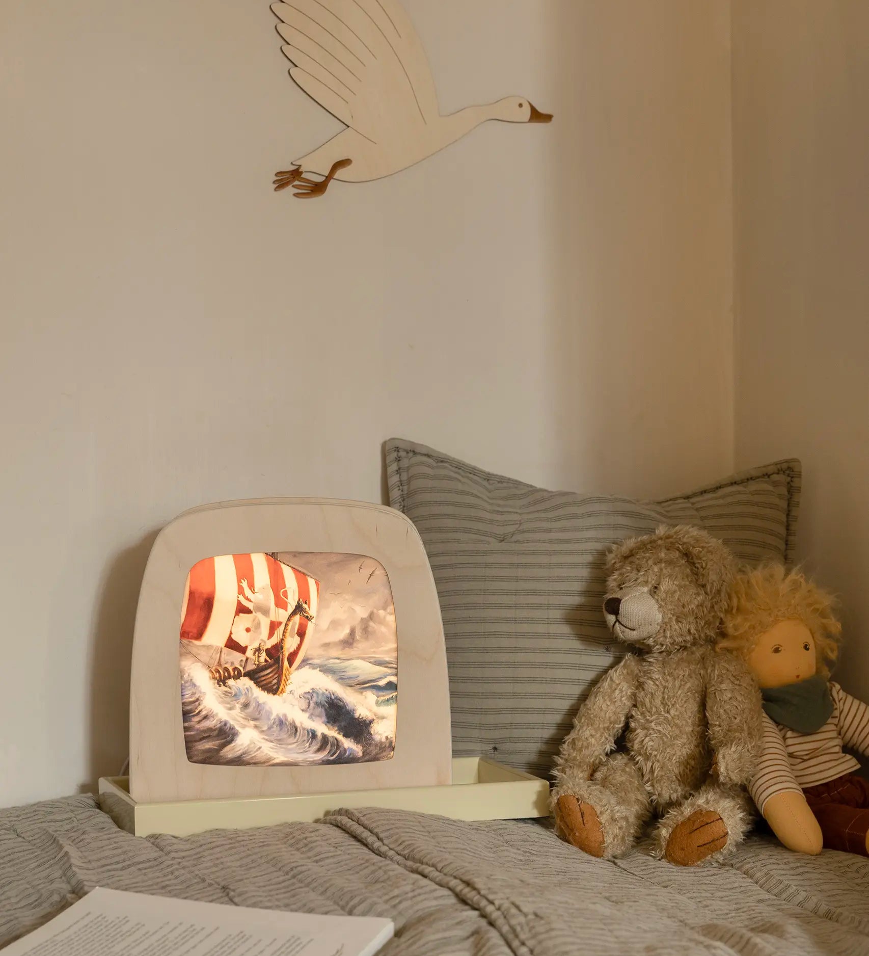 Toverlux Magic Lamp with artwork by Berit Strasser showing a Viking Ship sailing through the sea, on a child's bed next to a teddy bear and Nanchen Waldorf doll.